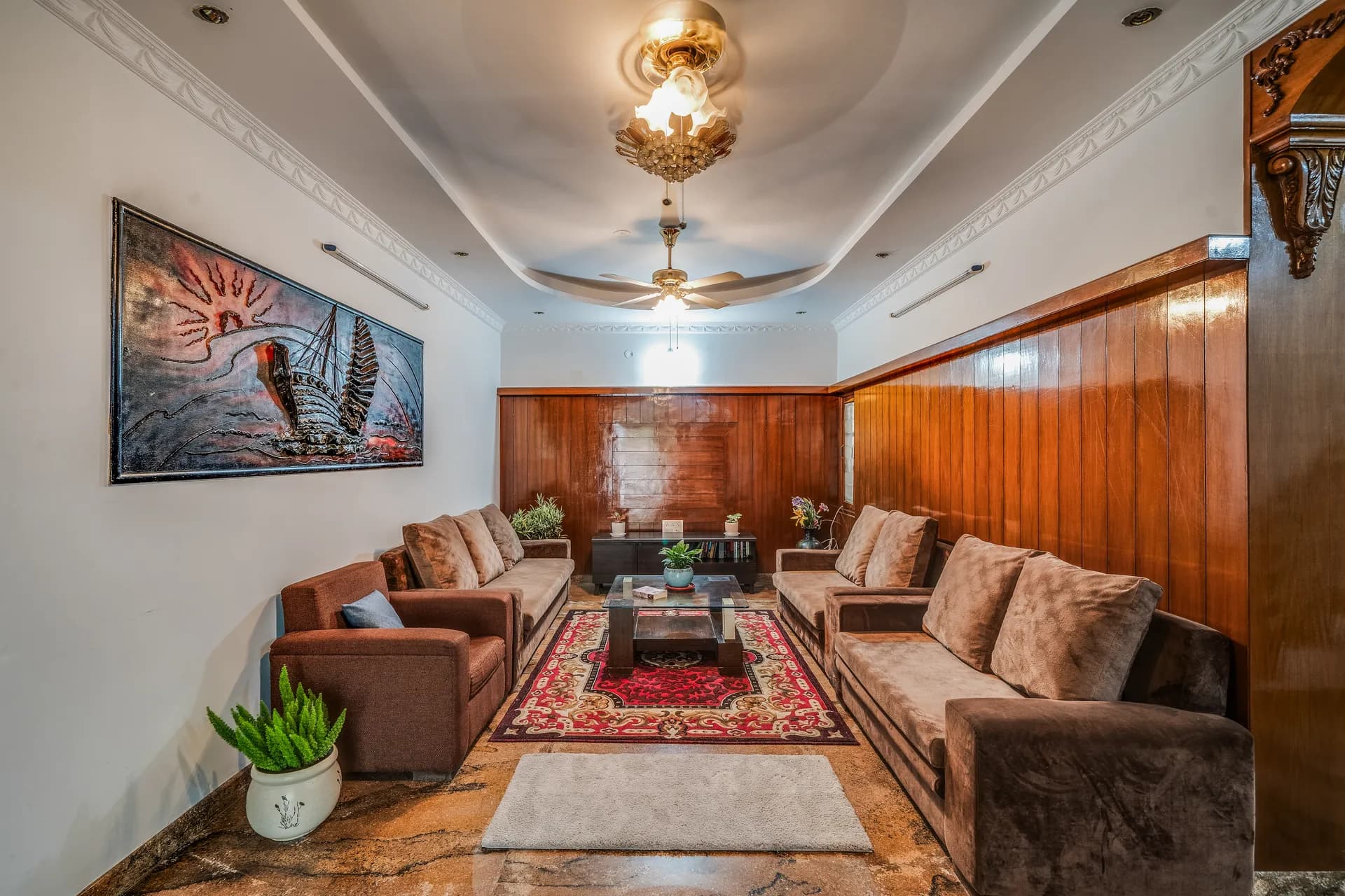 Formal living room with brown velvet sofas, red patterned rug, wood-paneled walls and a large framed painting.